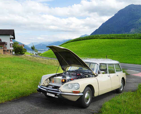 citroends23break_galerie28 Beige Citroen DS Break steht mit offener Motorhaube auf einem Einfahrtssträsschen im Grünen. Statt des Motors sieht man eine Batteriekiste. Im Hintergrund die Rigi.