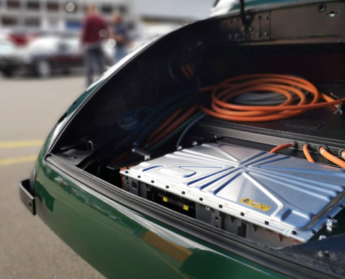 swissclassicworld2021_9 Das Heck eines grünen Jaguar XK 150, ohne Kofferraumklappe. Man sieht ein Ladegerät und orange Kabel.