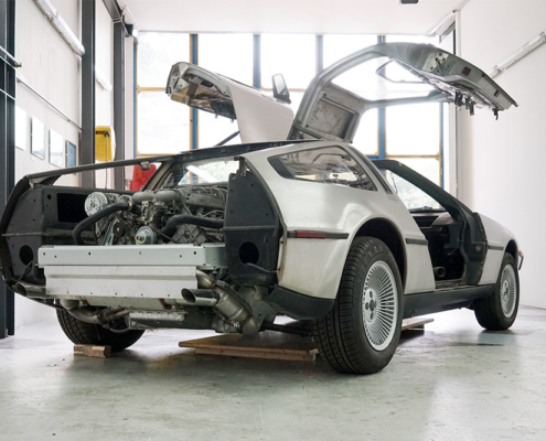 DSC06384_deLorean_manufakturmarton_gallerie1 Heckansicht eines DeLorean DMC-12, leicht schräg. Die Stossstange fehlt, ebenso die Heckklappe. Daher sieht man einen Teil des Rahmens sowie den Motor.