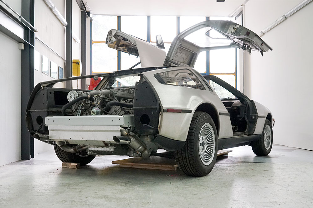 DSC06384_deLorean_manufakturmarton_gallerie1 Heckansicht eines DeLorean DMC-12, leicht schräg. Die Stossstange fehlt, ebenso die Heckklappe. Daher sieht man einen Teil des Rahmens sowie den Motor.