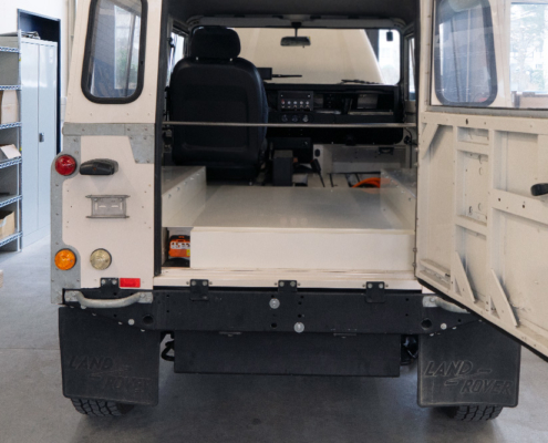 dEfender_manufakturmarton_galerie_04574 Das Heck eines Land Rover Defenders, mit Sicht auf die Ladefläche. Die Batteriekiste in Wagenfarbe findet auf der Ladefläche platz.