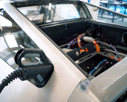Heck des DeLoreans, ein CCS-Stecker ist am hinteren Ende des hinteren Seitenfensters eingesteckt. Er passt gerade knapp in die Lücke, die sich in dem Bereich ergibt.