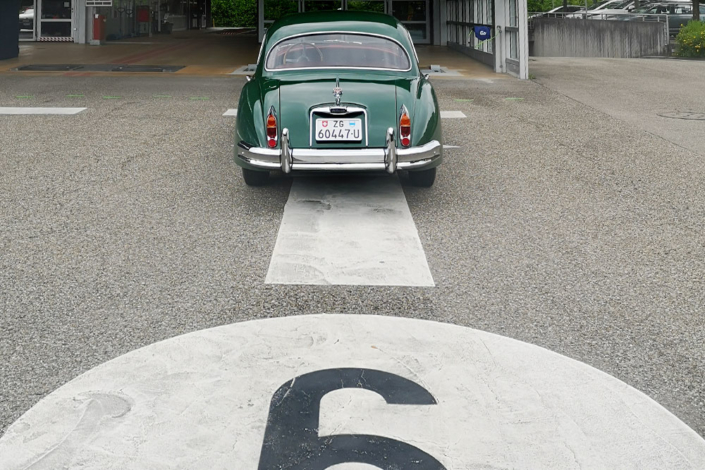 Jaguar XK 150 vor Strassenverkehrsamt Ein grüner Jaguar XK 150 steht auf einer Prüfbahn des Strassenverkehrsamtes Zug. Ansicht von Hinten auf das Auto. Man erkennt die Bahnnummer 6 im Bild unten, etwas angeschnitten.