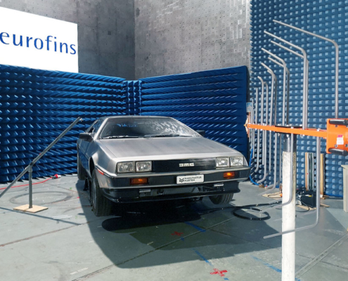 EMV Prüfung DeLorean Ein DeLorean wird gerade auf seine elektromagnetische Verträglichkeit geprüft. Er steht in einer Prüfhalle, eine orange-graue Antenne ist auf ihn gerichtet. Antenne im Vordergrund, Fahrzeug im Hintergrund, von leicht schräg vorne fotografiert.