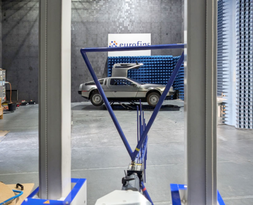 EMV Prüfung DeLorean Ein DeLorean wird gerade auf seine elektromagnetische Verträglichkeit geprüft. Er steht in einer Prüfhalle, eine blaue Antenne ist auf ihn gerichtet und misst seine elektromagnetischen Strahlungswerte. Man sieht das Fahrzeug im Hintergrund und die Antenne im Vordergrund.
