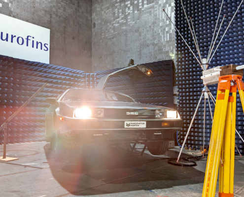 EMV Prüfung DeLorean Ein DeLorean wird gerade auf seine elektromagnetische Verträglichkeit geprüft. Er steht in einer Prüfhalle, eine Antenne auf gelbem Stativ ist auf ihn gerichtet und emittiert Strahlung, um seine Immunität zu testen.