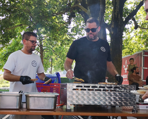 IMG_20240901_131632_blog Zwei Männer am Grillstand. Einer wendet gerade ein Burger Patty.