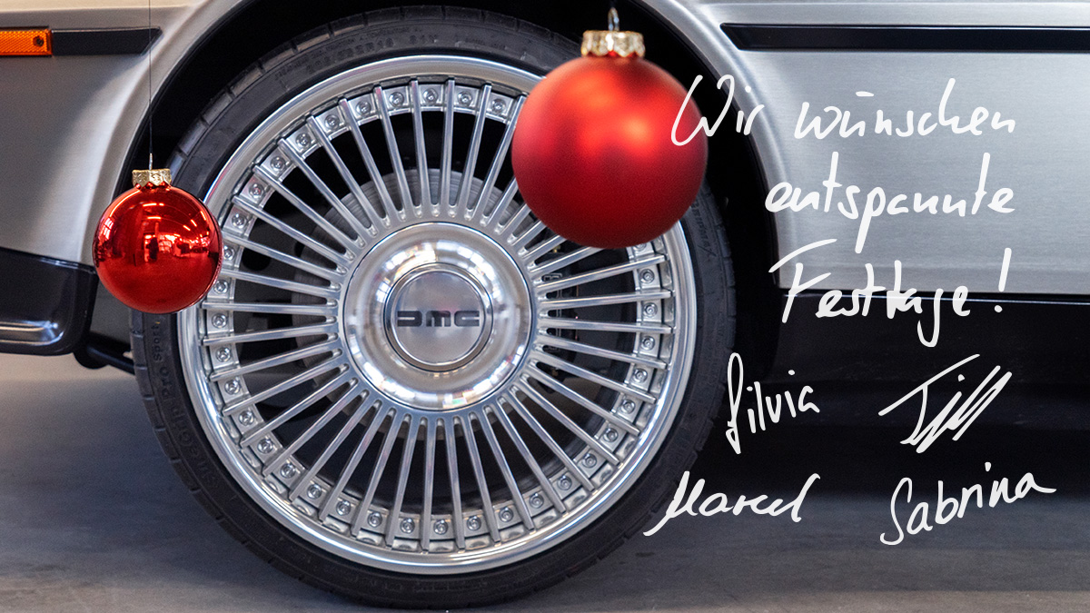 Festtage20242025 Bild eines Rads an einem Fahrzeug. Die Felge hat ein Speichen-Design, ein DMC-Logo verdeckt die Radmuttern. Vor dem Rad hängen zwei rote Christbaumkugeln ins Bild, eine davon matt, eine glänzend. Auf dem Bild steht zudem die hangeschriebene Nachricht "Wir wünschen frohe Festtage". Darunter die Unterschriften von Silvia, Till, Marcel und Sabrina.