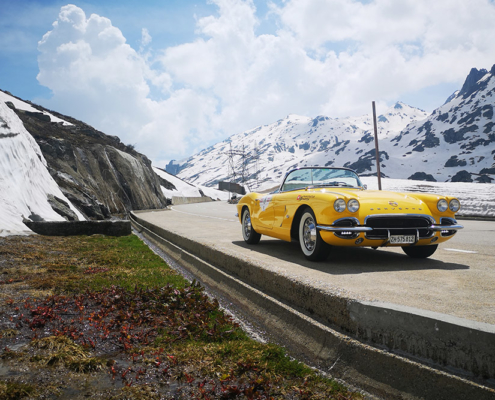 Corvette auf dem Gotthard-Pass Eine gelbe Corvette ist am Rande einer Passstrasse parkiert. Links hat es einen Schneewall, im Hintergrund eine leicht verschneite Berglandschaft.