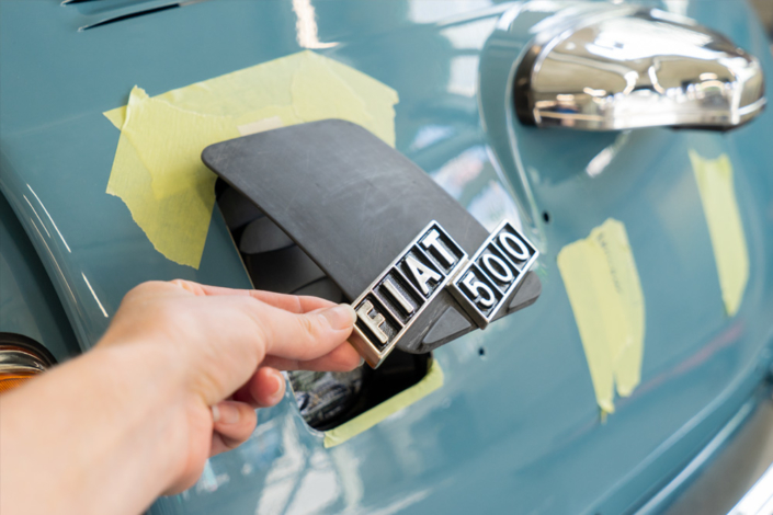 DSC09132_manufakturmartin_ladedose_blog Ladeklappe, noch roh und schwarz, mit originalem Fiatschriftzug für den elektrifizierten Fiat 500. Eine Hand hält sie etwas offen.