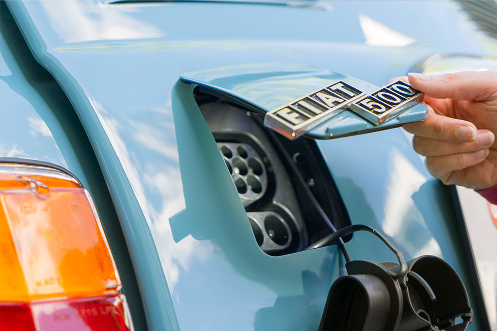 DSC00602_manufakturmarton_webgallerie Eine Öffnung am Heck des blau lackierten Fiat 500, die mit einer Klappe in Wagenfarbe verschlossen werden kann. Im Bild ist diese halb geöffnet, an ihr ist das Logo "Fiat 500" angebracht.