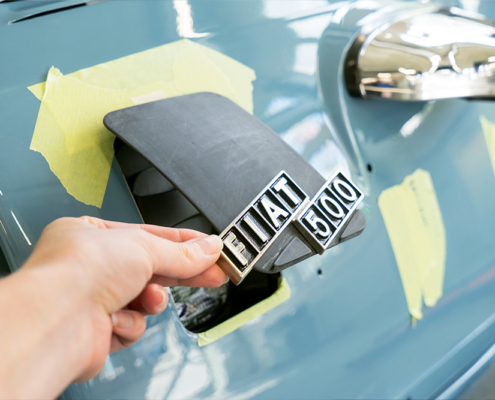 DSC09132_manufakturmarton_webgallerie Eine Öffnung am Heck des blau lackierten Fiat 500, die mit einer Klappe aus Kunststoff verschlossen werden kann. Im Bild ist diese halb geöffnet, an ihr ist das Logo "Fiat 500" angebracht.